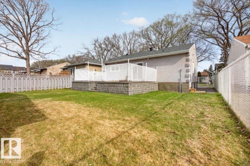 Expansive grassy yard with a raised patio featuring white lattice railing - 9723 65 Avenue, Edmonton, AB - Outdoor