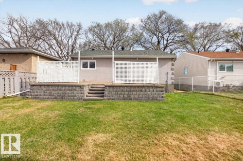 Expansive backyard featuring a tiered retaining wall, a raised concrete patio, and white lattice privacy screens - 9723 65 Avenue, Edmonton, AB - Outdoor