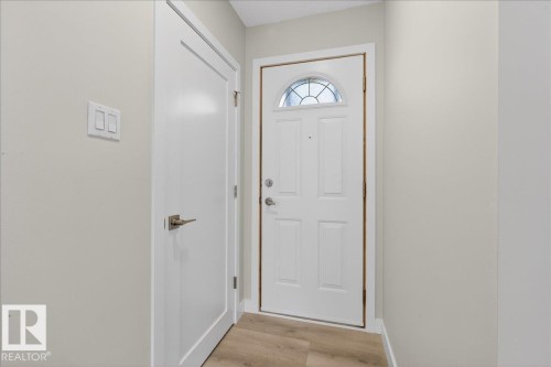 Entryway featuring a paneled white door with an arched glass insert, a second white door with brushed nickel hardware, light wood-finish flooring, and light-toned walls - 9723 65 Avenue, Edmonton, AB - Indoor Photo Showing Other Room