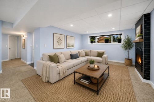 Finished living space featuring light blue walls, recessed lighting, a modern gas fireplace with black subway tile surround and wood mantel, a window with exterior visibility, and carpeting - 126 Harrison Drive, Edmonton, AB - Indoor Photo Showing Living Room