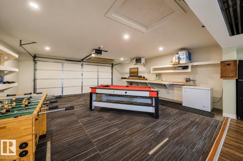 Versatile garage space featuring patterned floor tiles, overhead lighting, an overhead garage door, built-in shelving, and a workbench area - 126 Harrison Drive, Edmonton, AB - Indoor Photo Showing Garage