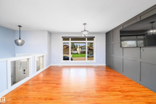 Open-concept living area with wood-finish flooring, a contemporary accent wall, and a large picture window - 126 Harrison Drive, Edmonton, AB - Indoor