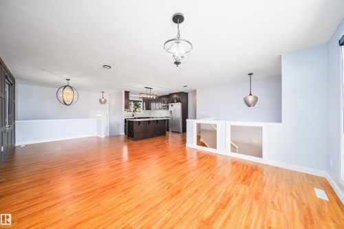 Spacious main level featuring wood-finish flooring throughout, a modern kitchen with dark cabinetry and stainless steel appliances, and contemporary pendant lighting fixtures - 126 Harrison Drive, Edmonton, AB - Indoor