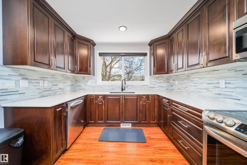 U-shaped kitchen featuring wood-finish cabinetry, light countertops, and a full tile backsplash - 126 Harrison Drive, Edmonton, AB - Indoor Photo Showing Kitchen With Upgraded Kitchen