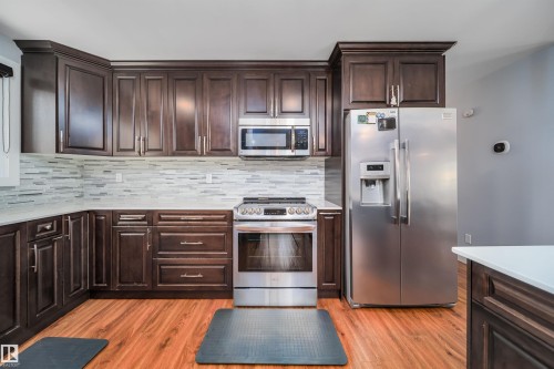 Kitchen featuring rich wood cabinetry, stainless steel appliances, a tile backsplash, and light-toned countertops - 126 Harrison Drive, Edmonton, AB - Indoor Photo Showing Kitchen With Upgraded Kitchen
