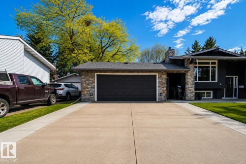 Contemporary exterior featuring a stone facade, a dark garage door, and ample concrete driveway - 126 Harrison Drive, Edmonton, AB - Outdoor With Facade