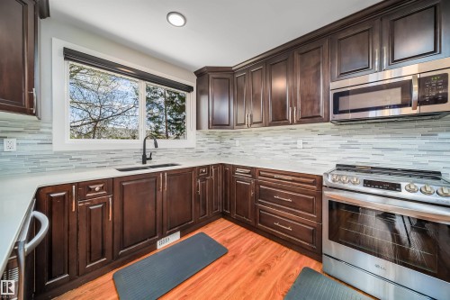 U-shaped kitchen featuring wood-finish cabinetry, light countertops, and a full tile backsplash - 126 Harrison Drive, Edmonton, AB - Indoor Photo Showing Kitchen