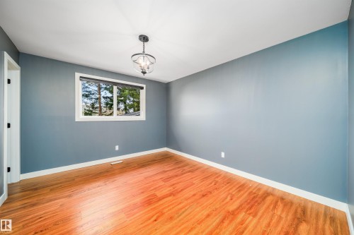 Bright interior space featuring wood-finish flooring, a contemporary ceiling light fixture, a window with exterior tree scenery, and white baseboards - 126 Harrison Drive, Edmonton, AB - Indoor Photo Showing Other Room