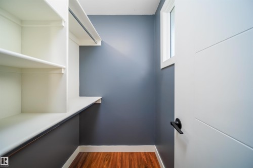 Walk-in closet featuring white shelving, a hanging rod, wood-finish flooring, a contemporary white door, and a high window - 126 Harrison Drive, Edmonton, AB - Indoor