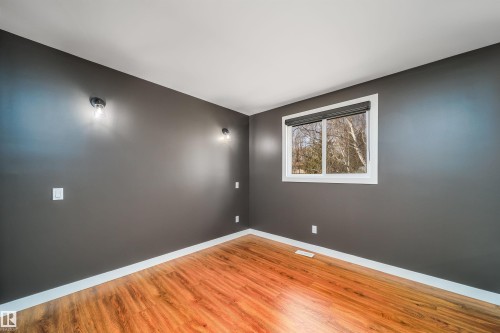 Room featuring wood-finish flooring, a window with a roller shade, dark gray walls, white trim, and wall-mounted light fixtures - 126 Harrison Drive, Edmonton, AB - Indoor Photo Showing Other Room