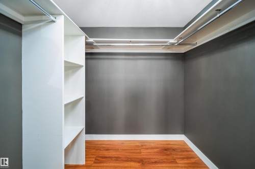 Walk-in closet featuring wood-finish flooring, built-in shelving, and multiple hanging rods - 126 Harrison Drive, Edmonton, AB - Indoor With Storage