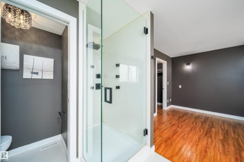 Glass-enclosed shower with matte black fixtures, an adjacent toilet, and wood-finish flooring extending into an additional room - 126 Harrison Drive, Edmonton, AB - Indoor