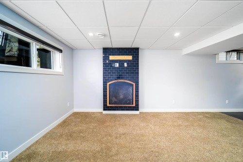Spacious room featuring a fireplace with dark blue subway tile surround, a built-in mantel, recessed lighting, and light brown carpet flooring - 126 Harrison Drive, Edmonton, AB - Indoor