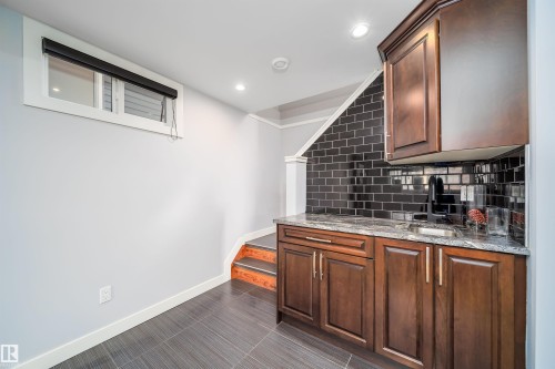 Wet bar featuring dark wood-finish cabinetry, a polished stone countertop, and a black subway tile backsplash - 126 Harrison Drive, Edmonton, AB - Indoor