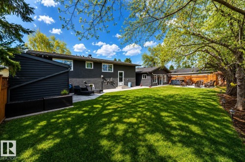 Expansive backyard featuring a manicured lawn, established shade trees, and a wooden privacy fence - 126 Harrison Drive, Edmonton, AB - Outdoor