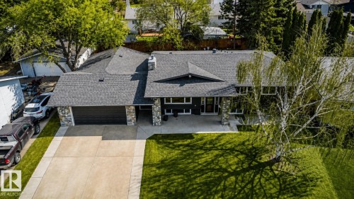 Contemporary style residence featuring a dark facade with stone accents, a multi-car driveway, attached garage, and a lush green lawn - 126 Harrison Drive, Edmonton, AB - Outdoor