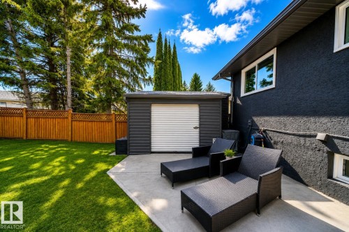 Expansive backyard featuring a concrete patio, detached storage shed with a roll-up door, and a wooden privacy fence - 126 Harrison Drive, Edmonton, AB - Outdoor With Exterior