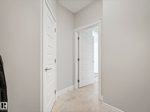 Hallway featuring light neutral wall paint, white five-panel interior doors, coordinating white trim, and beige tile flooring - 3817 Robins Crescent, Edmonton, AB - Indoor Photo Showing Other Room