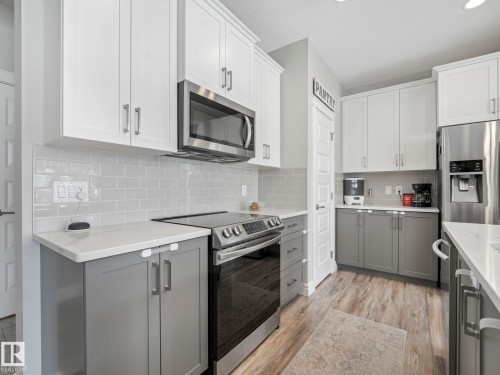 Modern kitchen featuring two-tone cabinetry, stainless steel appliances, light subway tile backsplash, and wood-finish flooring - 3817 Robins Crescent, Edmonton, AB - Indoor Photo Showing Kitchen With Stainless Steel Kitchen With Upgraded Kitchen