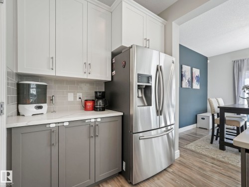 Kitchen area featuring white upper cabinetry and gray lower cabinetry, a stainless steel French door refrigerator with an ice and water dispenser, light-toned countertops, and a gray subway tile backsplash - 3817 Robins Crescent, Edmonton, AB - Indoor Photo Showing Kitchen