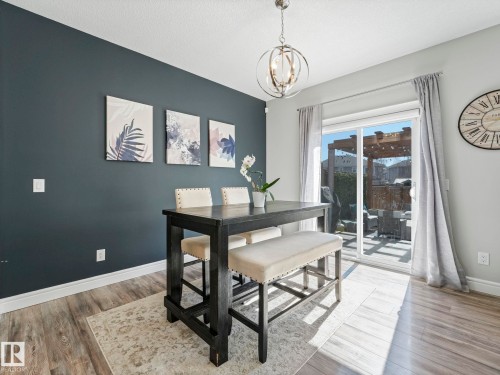 Dining area featuring wood-finish flooring, a contemporary overhead light fixture, and a sliding glass door leading to a patio with a pergola - 3817 Robins Crescent, Edmonton, AB - Indoor Photo Showing Dining Room