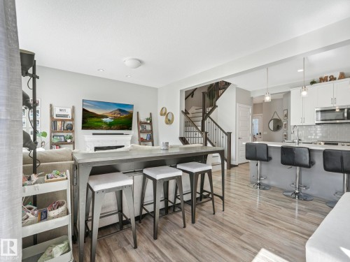 Open-concept living space featuring wood-finish flooring, a contemporary kitchen island with seating, a white subway tile backsplash, stainless steel appliances, and a staircase with dark wood railings - 3817 Robins Crescent, Edmonton, AB - Indoor Photo Showing Kitchen With Upgraded Kitchen