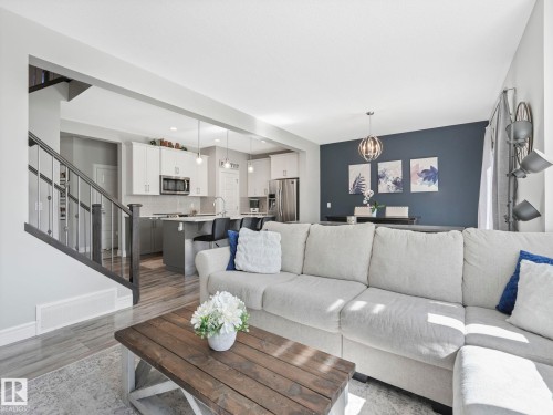 Open-concept living area featuring wood-finish flooring, a contemporary staircase with iron balusters, a kitchen with stainless steel appliances and pendant lighting, and a dining area with a modern chandelier - 3817 Robins Crescent, Edmonton, AB - Indoor Photo Showing Living Room