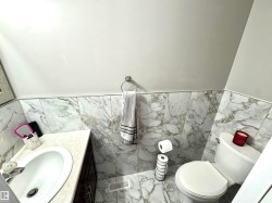 Half bath with vanity, a wainscoted wall, tile walls, and light marble finish floors - 