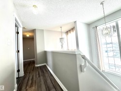 Hallway featuring hanging lights, a textured ceiling, dark wood-style flooring, and an upstairs landing - 