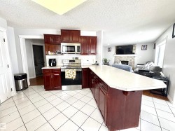 Kitchen featuring stainless steel appliances, a stone fireplace, light countertops, a peninsula, and reddish brown cabinets - 