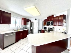 Kitchen featuring decorative backsplash, light countertops, a peninsula, bold wood finish cabinets, and a textured ceiling - 