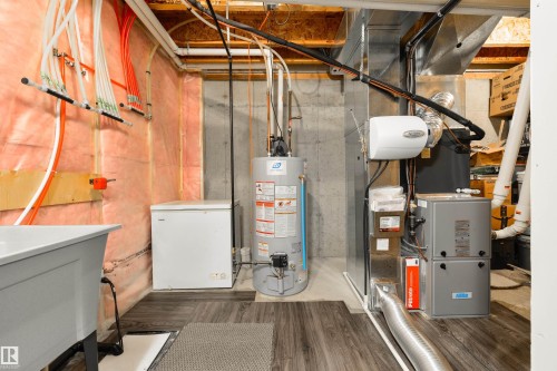 Utility area with wood-finish flooring, exposed insulation, a utility sink, and visible plumbing and HVAC systems - 4914 47 Street, Redwater, AB - Indoor Photo Showing Basement