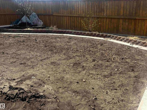 Expansive outdoor space featuring a wood fence perimeter, a curved brick-edged garden bed, a concrete border, and prepared soil for landscaping - 4914 47 Street, Redwater, AB - Outdoor