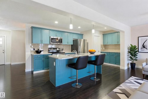 Kitchen featuring a central island with a light-toned countertop, teal cabinetry, stainless steel appliances, dark wood-finish flooring, and recessed lighting - 4914 47 Street, Redwater, AB - Indoor Photo Showing Kitchen With Upgraded Kitchen