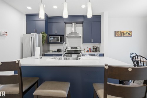 The kitchen features rich blue cabinetry, a stainless steel refrigerator, and a kitchen island with a white countertop - 4047 Hawthorn Link Link, Edmonton, AB - Indoor Photo Showing Kitchen With Upgraded Kitchen
