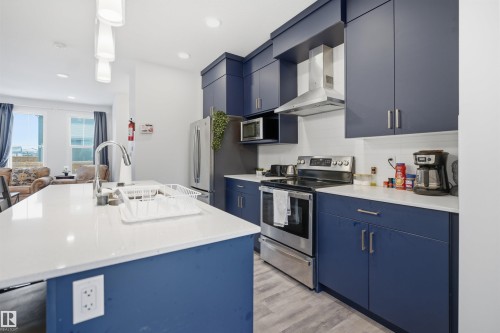 The kitchen features blue cabinetry, stainless steel appliances, and a central island with a sink and white countertop - 4047 Hawthorn Link Link, Edmonton, AB - Indoor Photo Showing Kitchen With Upgraded Kitchen