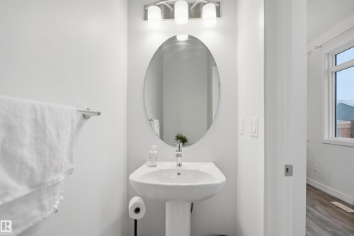 Bathroom featuring a pedestal sink, an oval mirror, and a modern light fixture - 4047 Hawthorn Link Link, Edmonton, AB - Indoor Photo Showing Bathroom