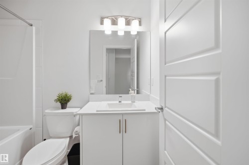 Bathroom featuring a vanity with a white countertop and white cabinetry, a sink with a chrome faucet, a large mirror, and a bathtub with white tile surround - 4047 Hawthorn Link Link, Edmonton, AB - Indoor Photo Showing Bathroom