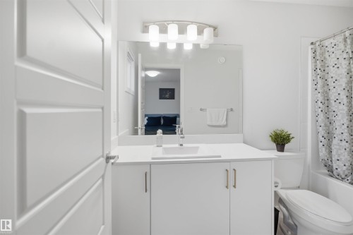 The bathroom features a vanity with a white countertop and sink, a mirror, and a shower with a patterned curtain - 4047 Hawthorn Link Link, Edmonton, AB - Indoor Photo Showing Bathroom