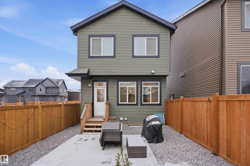 The property features green siding with black trim, a wooden deck, and a fenced yard with a concrete patio and gravel landscaping - 4047 Hawthorn Link Link, Edmonton, AB - Outdoor With Deck Patio Veranda