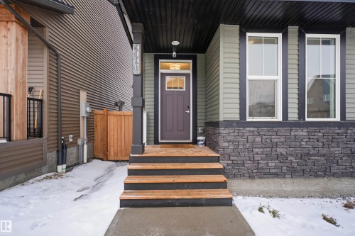 The property features a welcoming entrance with wooden steps and a dark brown door, complemented by light green siding and a stone-clad foundation - 4047 Hawthorn Link Link, Edmonton, AB - Outdoor