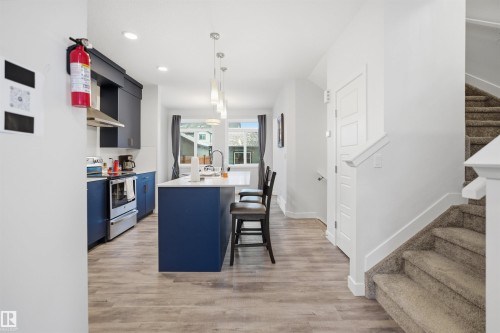 The kitchen features an island with seating, a stainless steel range, and blue lower cabinetry with dark upper cabinetry - 4047 Hawthorn Link Link, Edmonton, AB - Indoor Photo Showing Kitchen With Upgraded Kitchen