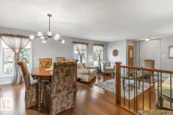 Open-concept living space featuring wood-finish flooring, a contemporary chandelier, multiple windows for natural light, and a wooden banister with wrought iron balusters - 