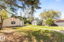 Expansive rear yard featuring a manicured lawn, established trees, and a utility shed - 