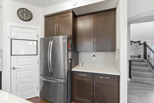 Contemporary kitchen featuring a stainless steel French door refrigerator, dark wood-finish cabinetry, light-toned countertops, and a white subway tile backsplash - 54 Cypress Link, Fort Saskatchewan, AB - Indoor Photo Showing Kitchen