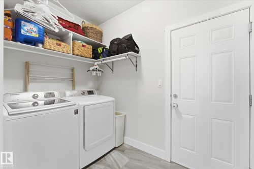 Utility area featuring a paneled door, overhead shelving, and wood-finish flooring - 54 Cypress Link, Fort Saskatchewan, AB - Indoor Photo Showing Laundry Room