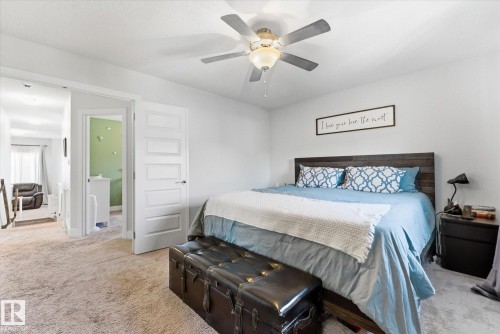 Carpeted room with a ceiling fan, a dark wood headboard, and two white five-panel interior doors - 54 Cypress Link, Fort Saskatchewan, AB - Indoor Photo Showing Bedroom