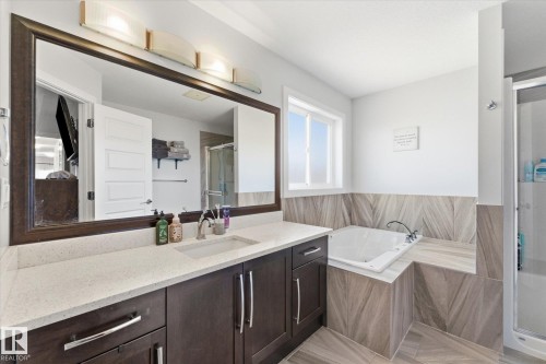 Bathroom featuring an integrated soaking tub, a dark wood-finish vanity with a light-toned countertop, and a large framed mirror with overhead lighting - 54 Cypress Link, Fort Saskatchewan, AB - Indoor Photo Showing Bathroom
