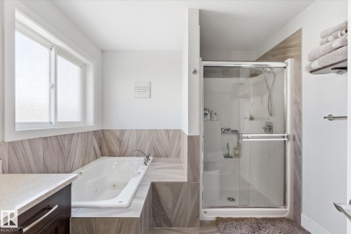 Bathroom featuring a deep soaking tub, glass-enclosed shower, frosted window, wood-finish tile accents, and a vanity with a light-toned countertop - 54 Cypress Link, Fort Saskatchewan, AB - Indoor Photo Showing Bathroom