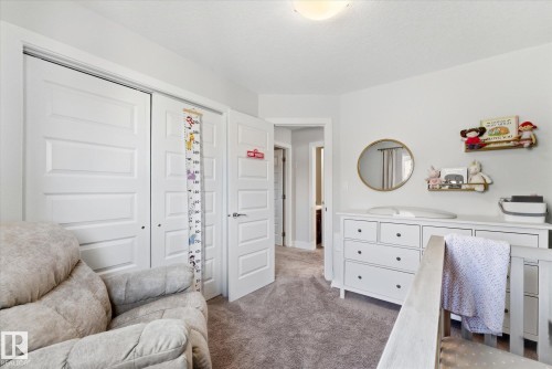 Carpeted room featuring a ceiling-mounted light fixture, white interior doors, and a round wall mirror - 54 Cypress Link, Fort Saskatchewan, AB - Indoor Photo Showing Bedroom